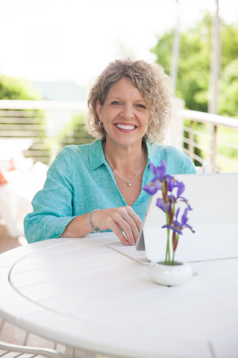 Image of Rhonda sitting outside at a table. She has her white laptop open and is smiling at the camera